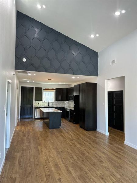 Kitchen with a kitchen breakfast bar, wood-type flooring, sink, a center island, and a towering ceiling