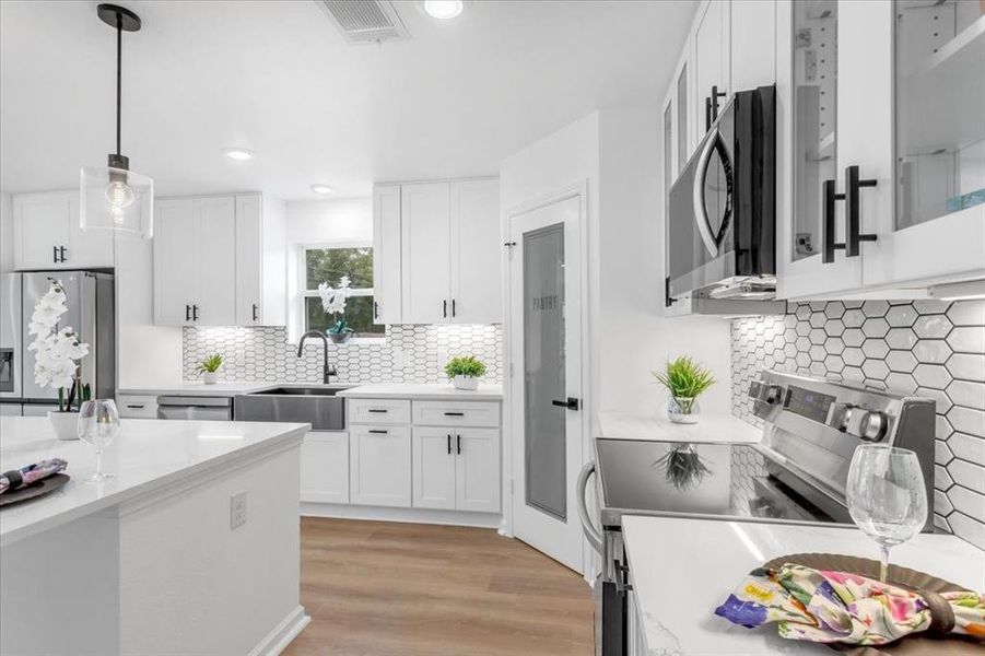 Kitchen featuring light wood-type flooring, decorative light fixtures, sink, white cabinets, and appliances with stainless steel finishes