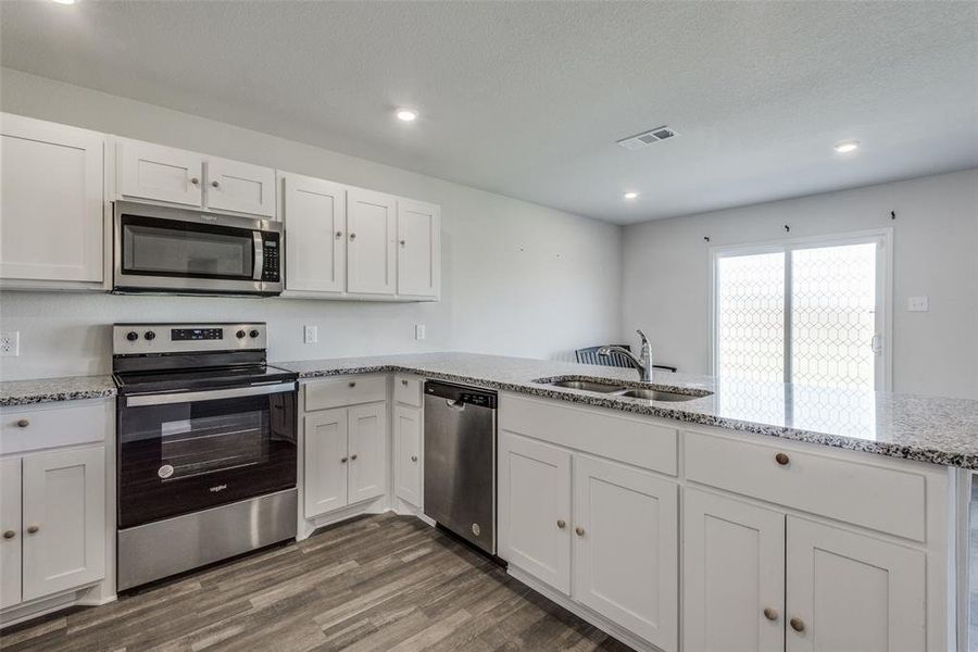 Kitchen with dark hardwood / wood-style floors, sink, white cabinets, kitchen peninsula, and stainless steel appliances