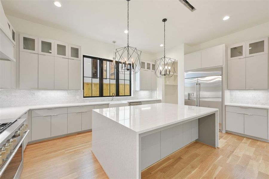 Another view of the island kitchen. storage abound with cabinets on both sides of the island, glass front upper cabinets and large slab front cabinets below. The two pendent lights are supported by undercabinet lighting and recessed LED fixtures. The mud room leads to the garage entry and large walk-in pantry.