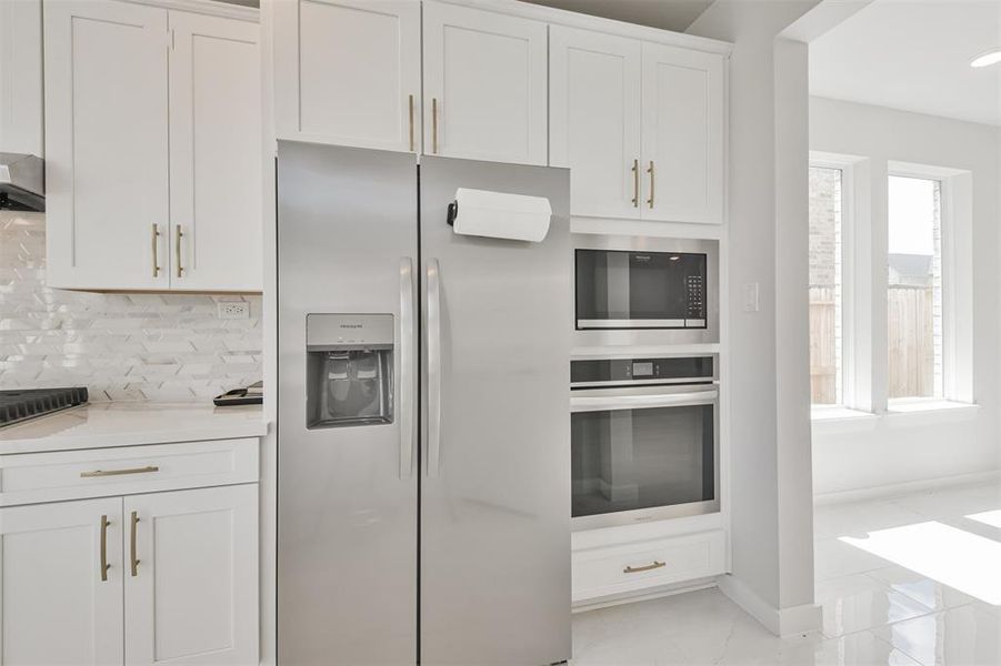 This is a modern kitchen with stainless steel appliances, white cabinetry, and a stylish backsplash, complemented by natural light from the window.