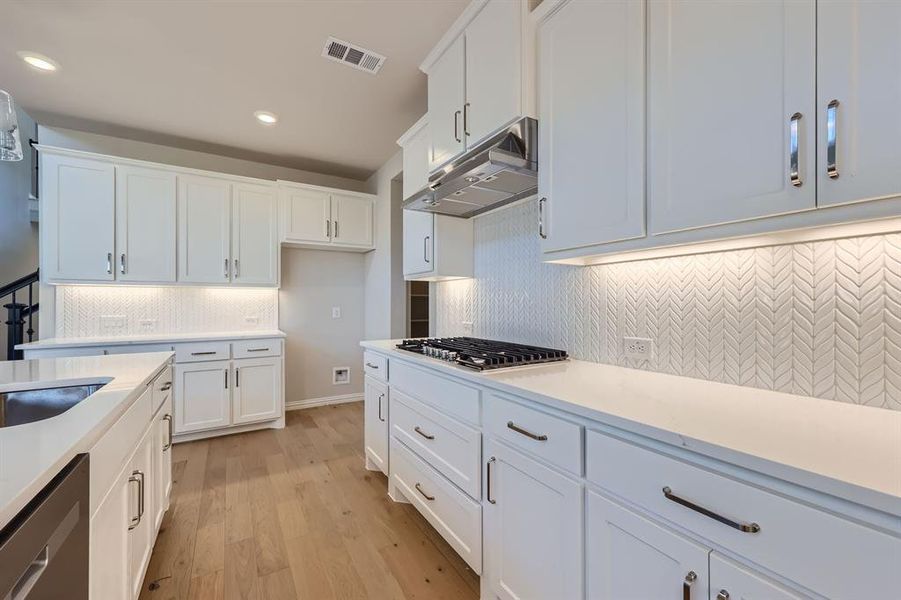 Kitchen featuring tasteful backsplash, sink, white cabinetry, light hardwood / wood-style floors, and stainless steel appliances