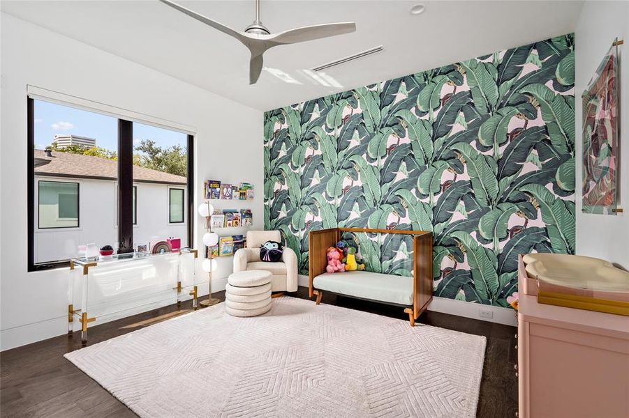 This charming secondary bedroom features a vibrant Beverly Hills Hotel Iconic Banana Leaf wallpaper that adds a playful and lively atmosphere. The room is complemented by large windows that allow for ample natural light, while a ceiling fan ensures comfort.