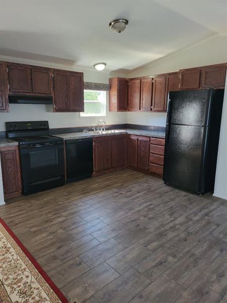 Kitchen with dark wood-type flooring, black appliances, lofted ceiling, and sink