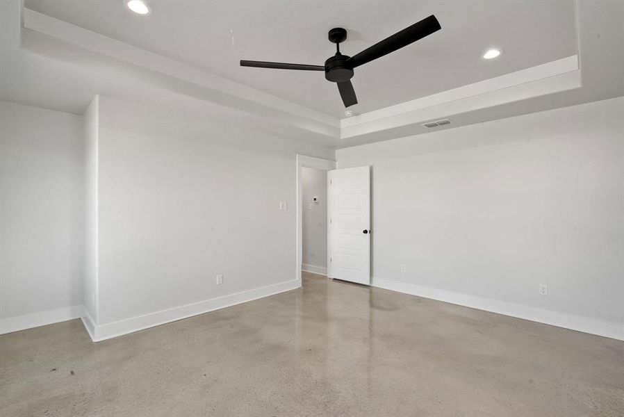 Bedroom with a raised ceiling, concrete flooring, and ceiling fan