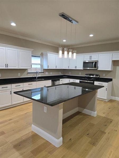 Kitchen with light wood-type flooring, range, a kitchen island, and white cabinets