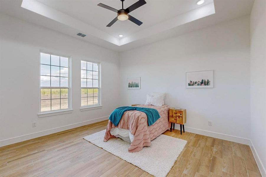 Bedroom with a raised ceiling, light hardwood / wood-style flooring, and ceiling fan