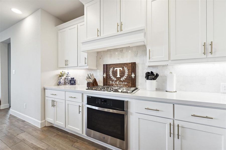 The cooktop is a 5 burner gas cooktop with the second oven located in the cabinet below. Quartz countertops are backed by a custom tile backsplash. Upper cabinets are 42" with crown molding and have undercabinet lighting that serves to brighten this spacious kitchen.