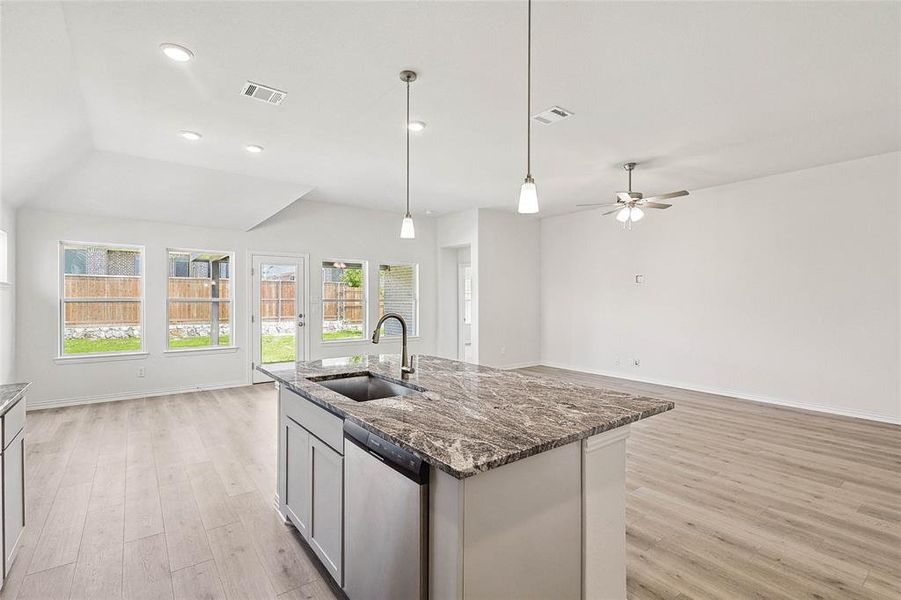 Kitchen featuring a kitchen island with sink, dark stone countertops, stainless steel dishwasher, light hardwood / wood-style flooring, and sink