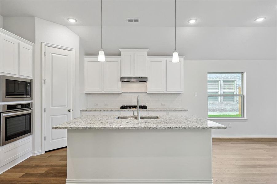 Kitchen featuring an island with sink, pendant lighting, stainless steel appliances, and white cabinets