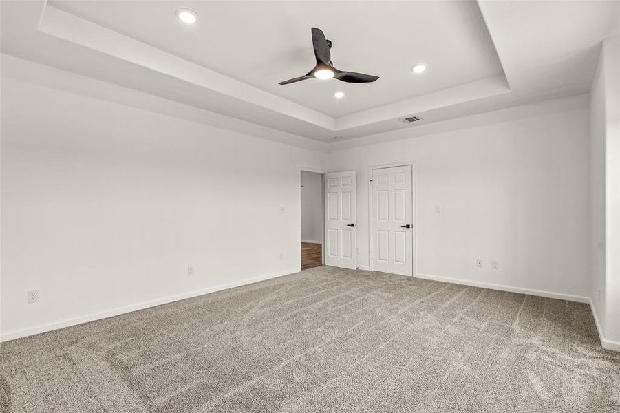 Unfurnished bedroom featuring ceiling fan, a raised ceiling, and carpet