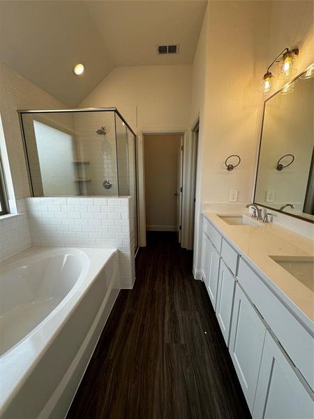 Bathroom with hardwood / wood-style flooring, independent shower and bath, double sink vanity, and vaulted ceiling