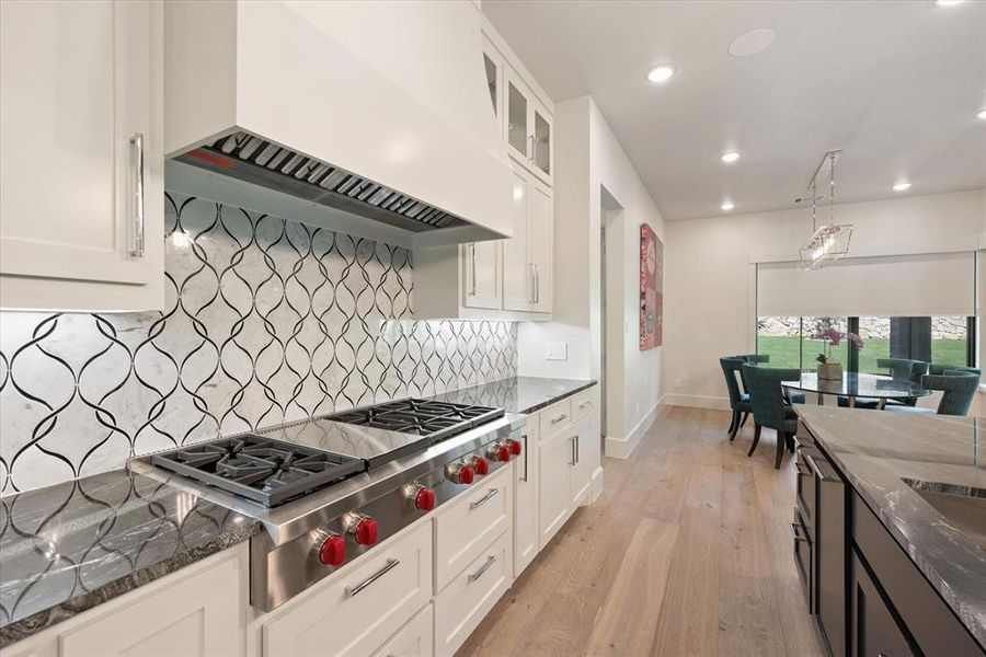 Kitchen featuring white cabinets, custom exhaust hood, light hardwood / wood-style floors, stainless steel gas cooktop, and dark stone counters