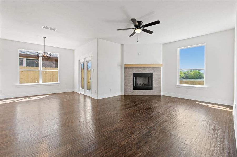 Unfurnished living room with dark wood-type flooring, ceiling fan with notable chandelier, and a fireplace