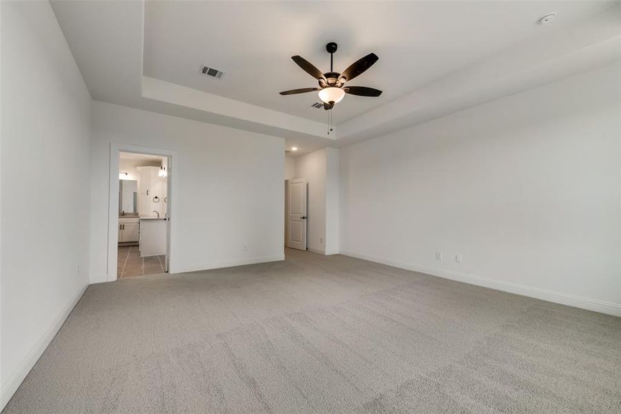 Unfurnished bedroom featuring light carpet, connected bathroom, ceiling fan, and a tray ceiling