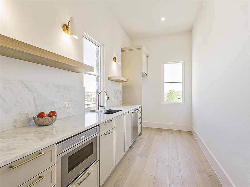 Kitchen featuring light stone counters, tasteful backsplash, sink, light hardwood / wood-style flooring, and appliances with stainless steel finishes