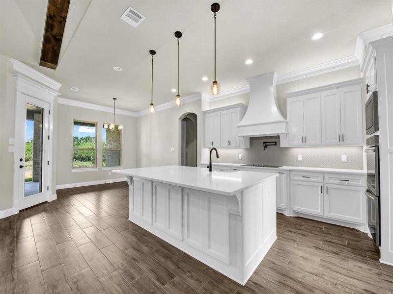 Kitchen featuring dark wood-type flooring, premium range hood, white cabinetry, and a kitchen island with sink