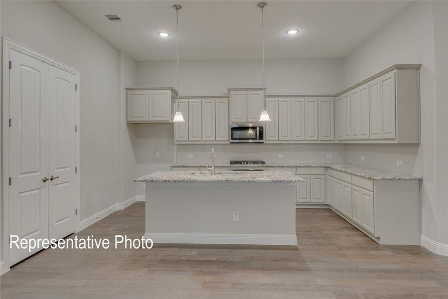 Kitchen featuring a kitchen island with sink, light stone countertops, pendant lighting, and light wood-type flooring