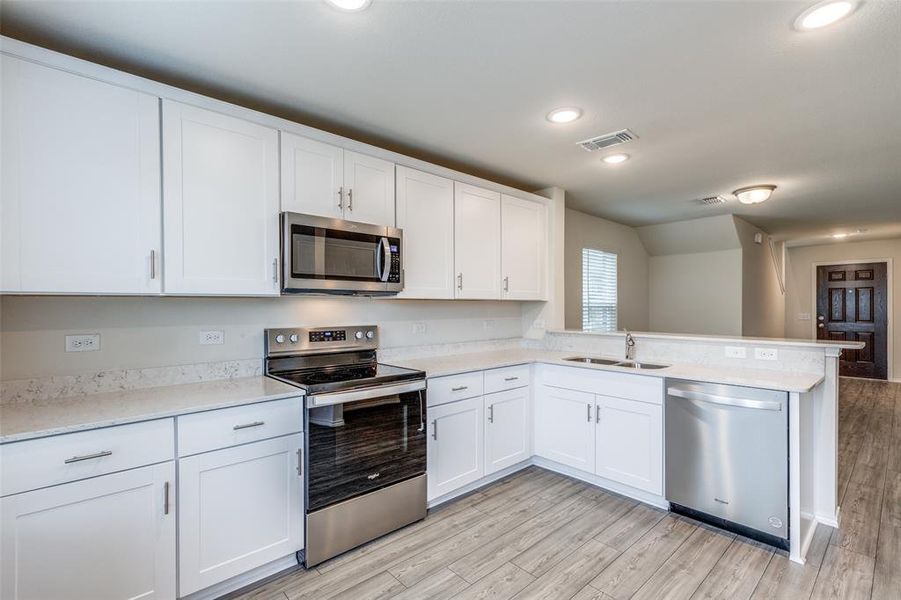 Kitchen featuring light hardwood / wood-style floors, appliances with stainless steel finishes, kitchen peninsula, and white cabinetry