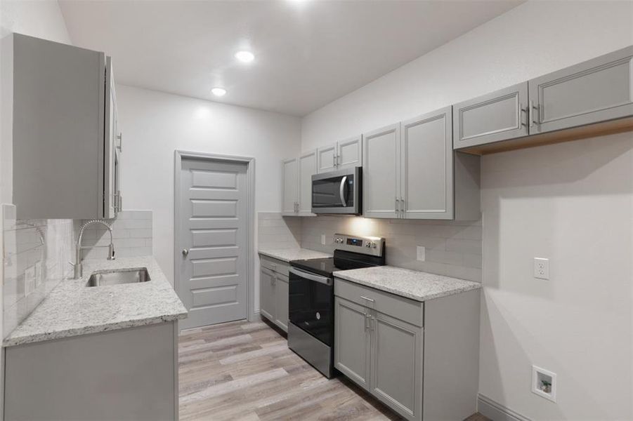 Kitchen featuring stainless steel appliances, backsplash, sink, and light wood-type flooring