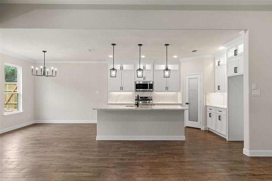 Kitchen with hanging light fixtures, a center island with sink, and dark wood-type flooring
