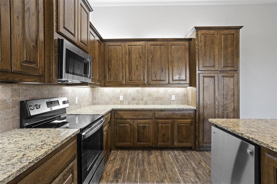 Kitchen with dark hardwood / wood-style flooring, stainless steel appliances, ornamental molding, and tasteful backsplash