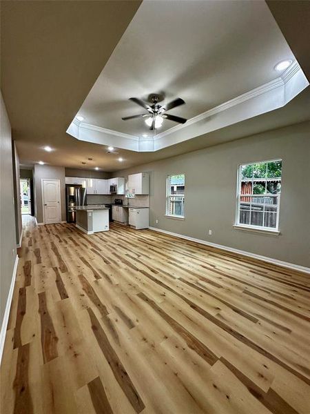 Unfurnished living room with ceiling fan, light hardwood / wood-style flooring, a raised ceiling, and a wealth of natural light