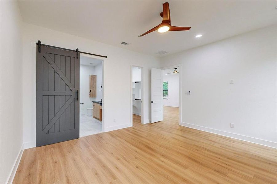 Unfurnished room with a barn door, light wood-type flooring, and ceiling fan