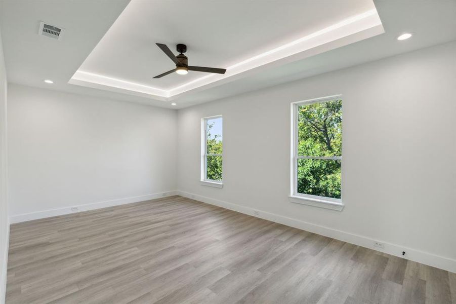 Bedroom with a healthy amount of sunlight, a tray ceiling, and light hardwood / wood-style flooring