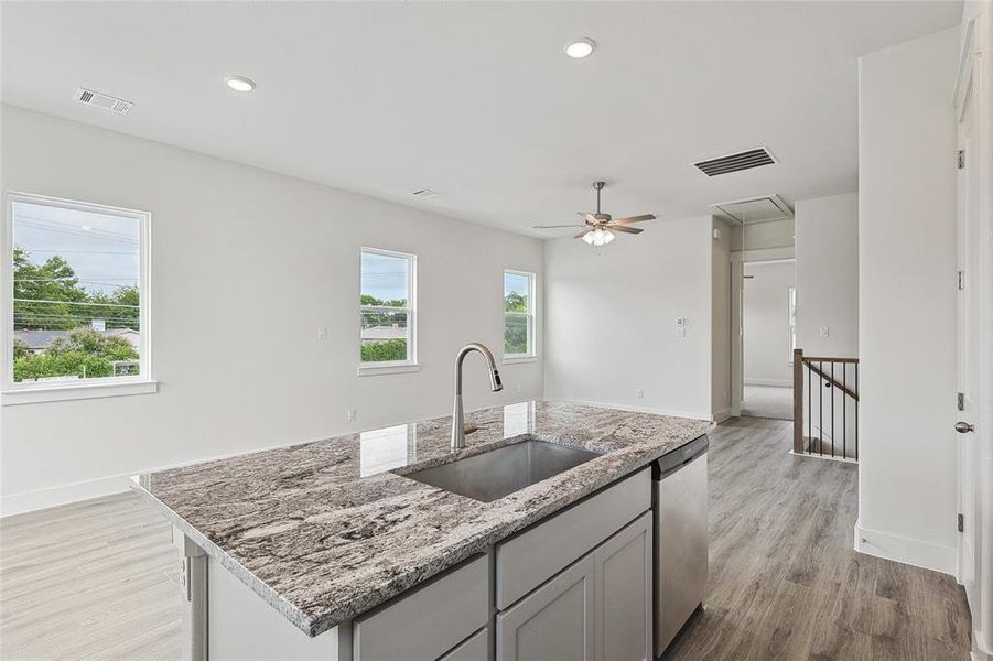 Kitchen with a center island with sink, sink, stainless steel dishwasher, light wood-type flooring, and light stone countertops