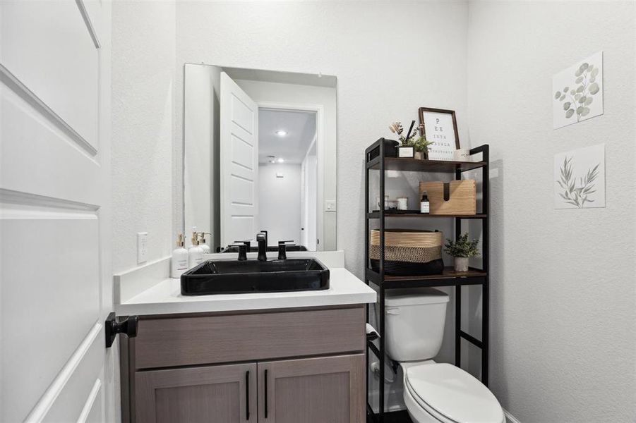 The modern, well-lit powder bathroom features a sleek vanity with a dark countertop, a large mirror, and a spacious storage shelf unit. The clean design and neutral colors give it a contemporary feel.