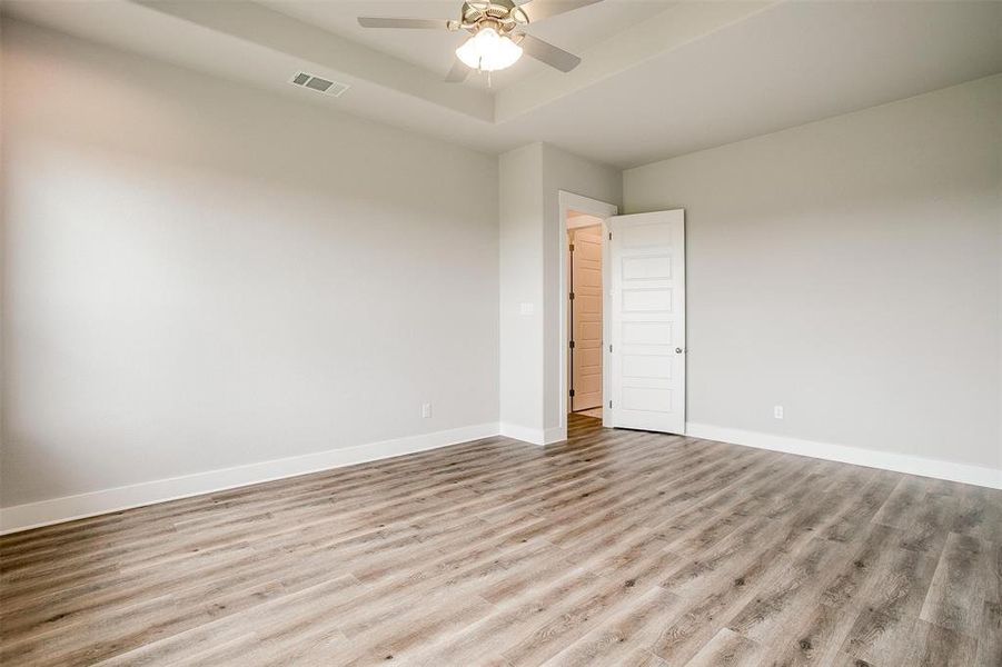 Empty room with a tray ceiling, ceiling fan, and light wood-type flooring