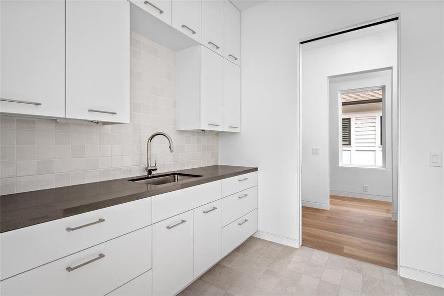 This centrally located second-floor laundry room offers dual-sided entry with convenient pocket doors. Featuring elegant gray limestone flooring, quartz countertops with a large sink, and dual-sided custom built-in cabinetry, this space is designed for both efficiency and style, making laundry tasks a breeze.