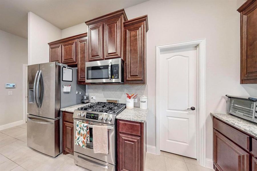 Kitchen featuring stainless steel appliances, light tile patterned flooring, light stone counters, and tasteful backsplash