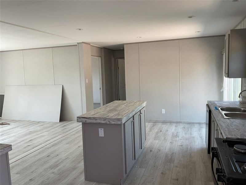 Kitchen with light hardwood / wood-style floors, black range with electric stovetop, a kitchen island, gray cabinets, and sink