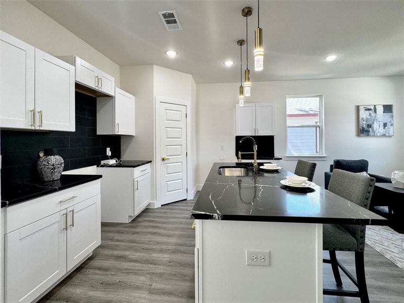 Kitchen featuring light hardwood / wood-style floors, a center island with sink, a kitchen bar, and white cabinets