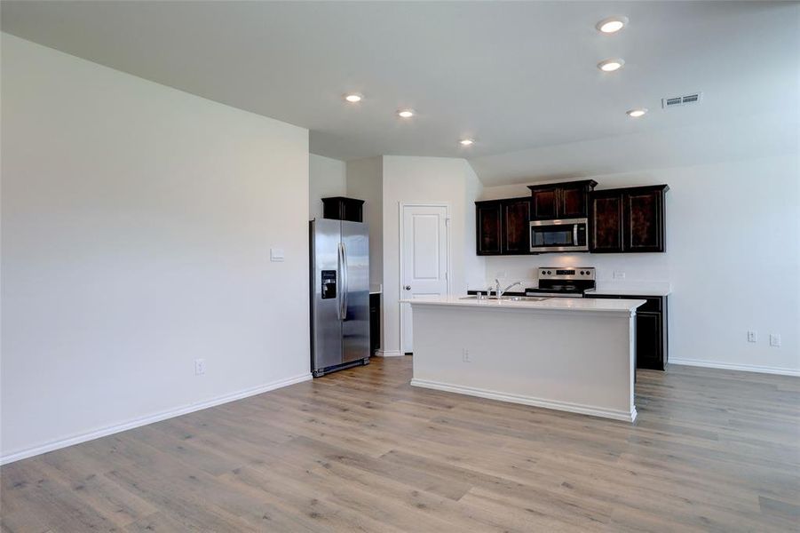 Kitchen with a center island with sink, appliances with stainless steel finishes, sink, and light hardwood / wood-style flooring