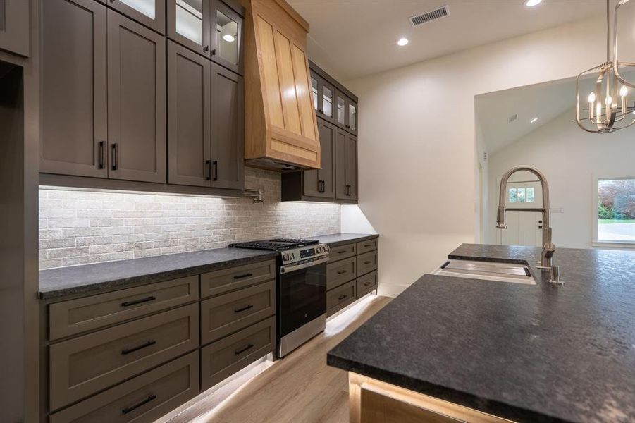 Kitchen with gas stove, tasteful backsplash, sink, light hardwood / wood-style floors, and custom exhaust hood