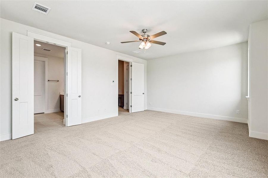 Unfurnished bedroom featuring ceiling fan, ensuite bathroom, and light carpet