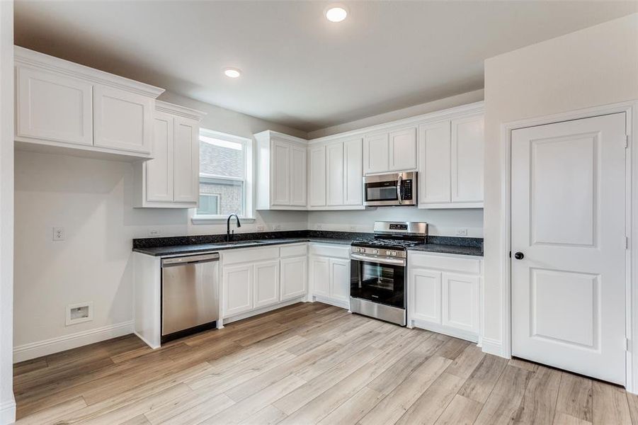 Kitchen with sink, white cabinets, light wood-type flooring, and appliances with stainless steel finishes