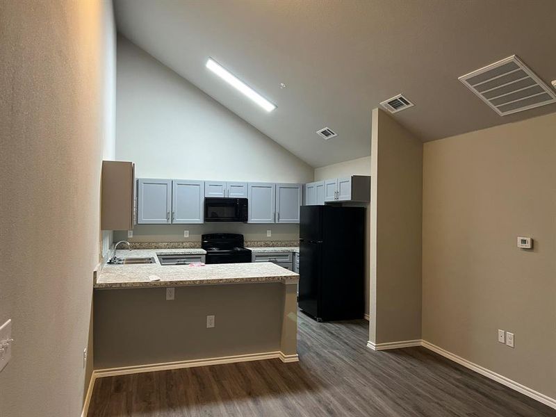 Kitchen with black appliances, kitchen peninsula, high vaulted ceiling, and dark wood-type flooring