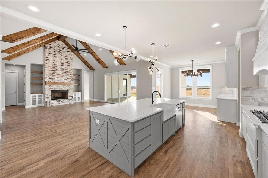 Kitchen featuring a spacious island, light wood-type flooring, vaulted ceiling with beams, a fireplace, and sink