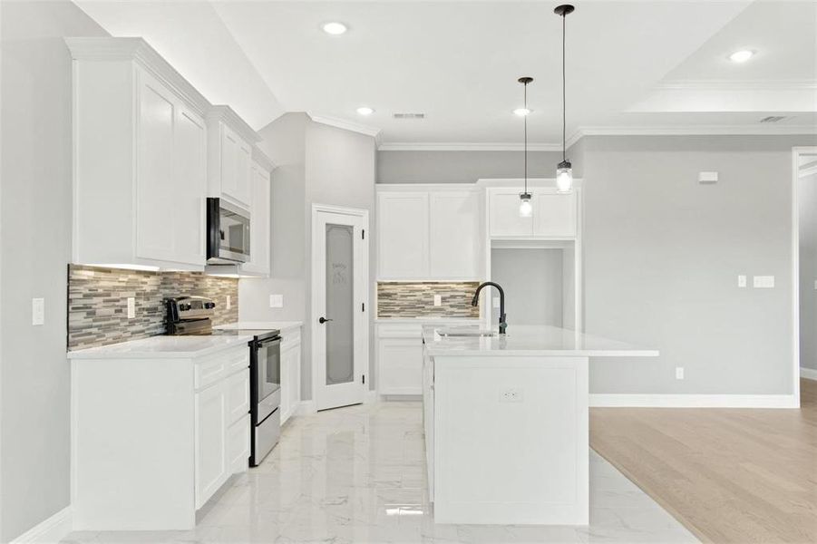 Kitchen featuring pendant lighting, stainless steel appliances, white cabinets, and a kitchen island with sink