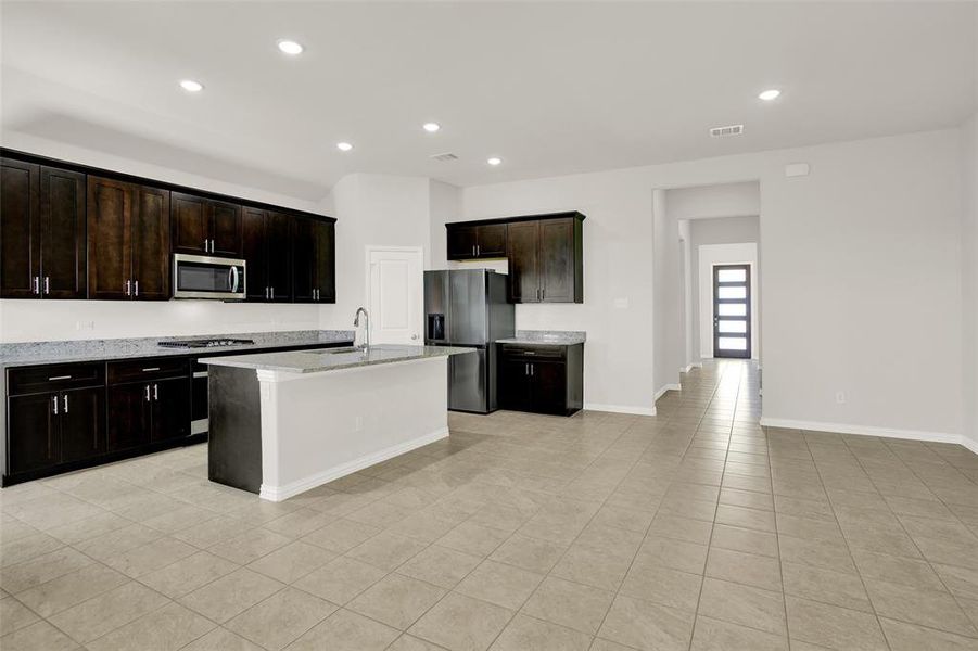 Kitchen with stainless steel appliances, a kitchen island with sink, light stone countertops, sink, and light tile floors