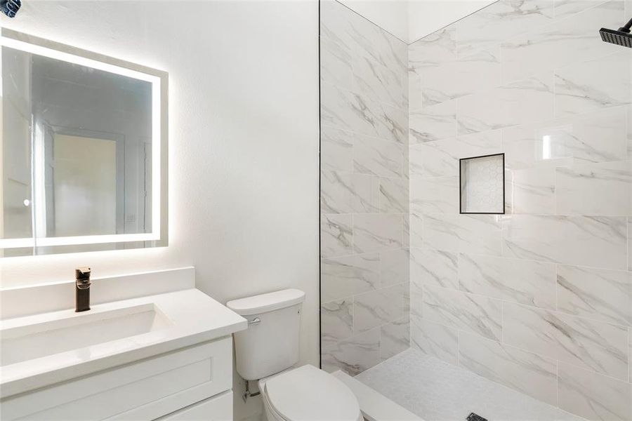 This is a modern bathroom featuring marble-like tiles, a glass shower enclosure with matte black hardware, and a sleek white vanity with quartz contertops.