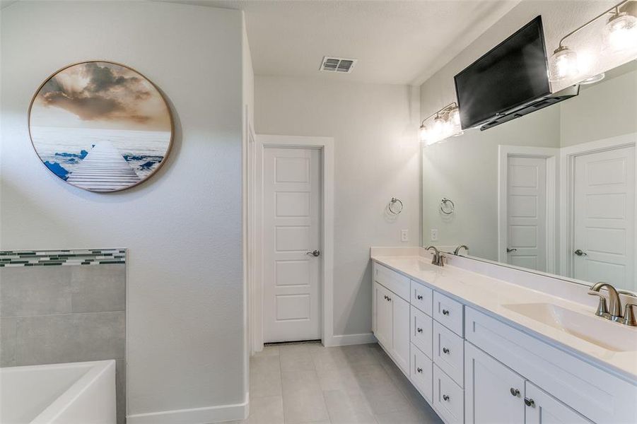 Primary bathroom with tile patterned floors, a tub, and vanity