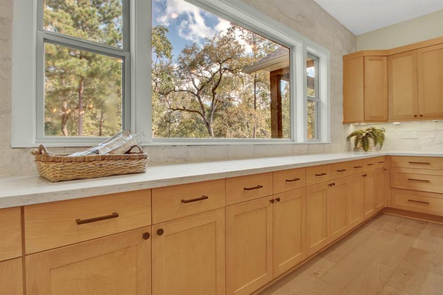 The beautiful picture window in the kitchen features natural light, a serene view of the trees out back, and ample wooden cabinetry with modern hardware.