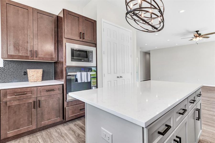 Kitchen with decorative backsplash, light wood-type flooring, ceiling fan with notable chandelier and appliances.