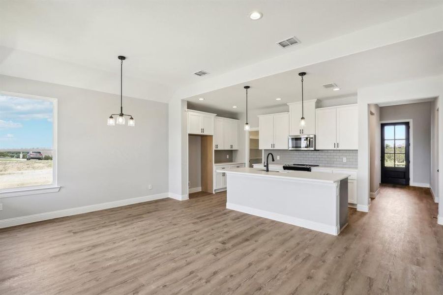 Kitchen featuring decorative backsplash, light hardwood / wood-style floors, decorative light fixtures, and a center island with sink