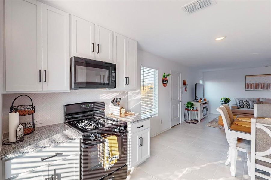 Kitchen featuring light stone counters, black appliances, light tile patterned flooring, white cabinetry, and backsplash